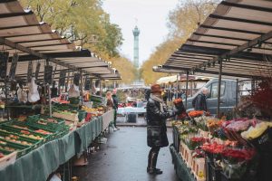 Woman shopping at Bastille’s Marché food market in Paris, surrounded by fresh produce and local vendors