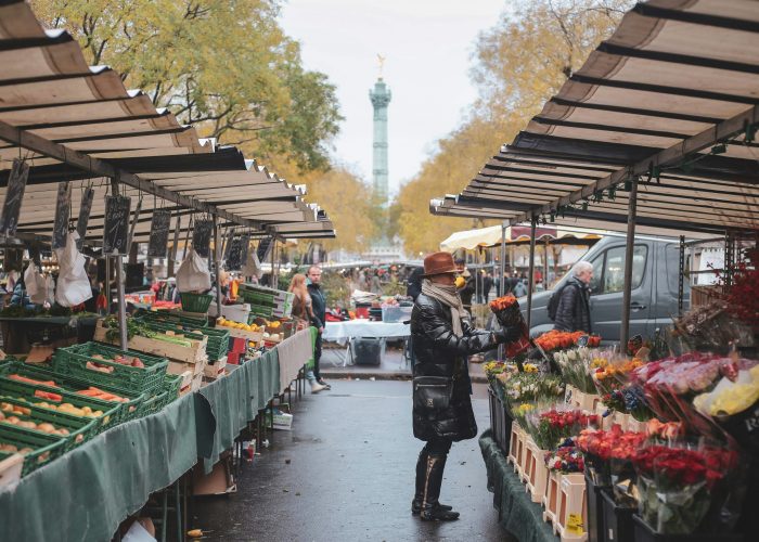 Woman shopping at Bastille’s Marché food market in Paris, surrounded by fresh produce and local vendors