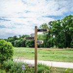 Wooden signpost with directions, surrounded by lush greenery in Burgundy, France under a bright summer sky. The beauty of traveling green.