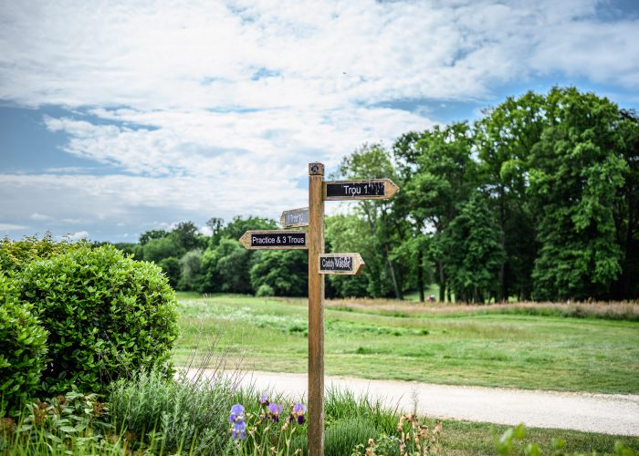 Wooden signpost with directions, surrounded by lush greenery in Burgundy, France under a bright summer sky. The beauty of traveling green.