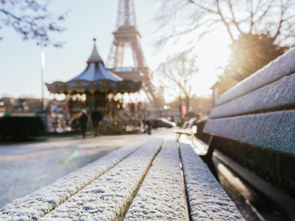 Wintertime in Paris: the Eiffel Tower in the background & bench coated in snow in the foreground.