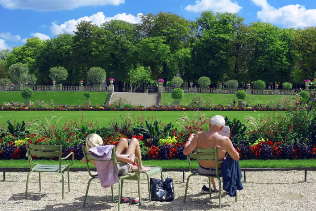 Parisians sitting on green chairs in the Jardin du Luxembourg.
