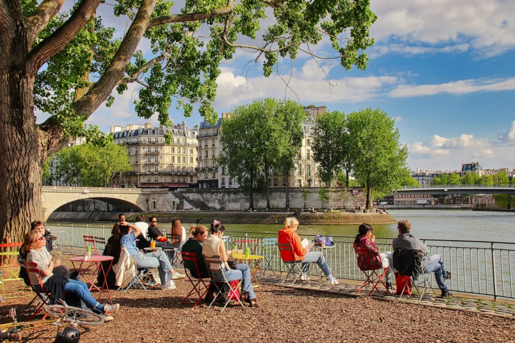 A group of people sitting on a terrace near the River Seine in Paris on a sunny day.