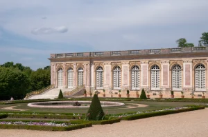Exterior of The Grand Trianon, overlooking its formal gardens, with ornate pink marble architecture and symmetrical flower beds