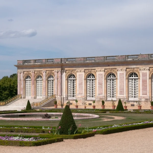 Exterior of The Grand Trianon, overlooking its formal gardens, with ornate pink marble architecture and symmetrical flower beds